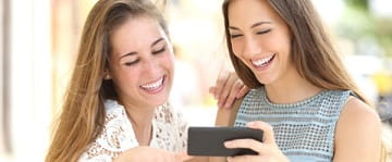 Junge Frauen schauen lachend auf Smartphone